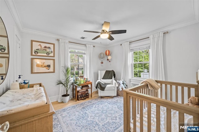 bedroom with multiple windows, a nursery area, ornamental molding, wood finished floors, and ceiling fan