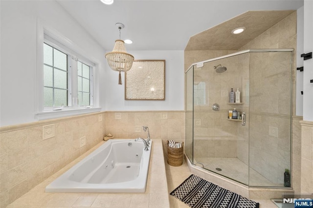 full bath featuring a stall shower, a jetted tub, a chandelier, a wainscoted wall, and tile walls