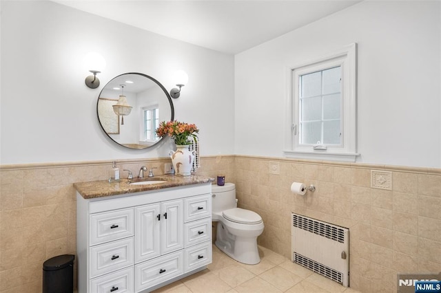 bathroom featuring radiator heating unit, tile walls, wainscoting, tile patterned flooring, and toilet