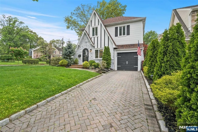 tudor house with a garage, decorative driveway, a front lawn, brick siding, and board and batten siding