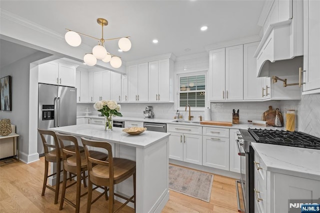 kitchen featuring stainless steel appliances, a sink, white cabinets, light wood-type flooring, and crown molding