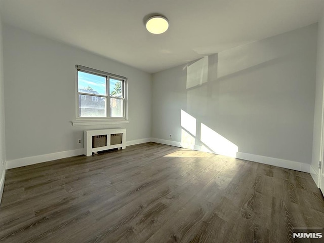spare room featuring radiator, dark wood-style floors, and baseboards