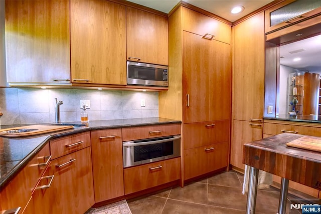 kitchen featuring appliances with stainless steel finishes, backsplash, dark tile patterned flooring, and dark stone counters