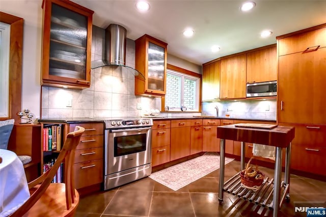 kitchen with wall chimney exhaust hood, stainless steel appliances, backsplash, recessed lighting, and brown cabinets