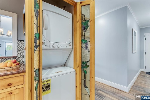 laundry area featuring estacked washer and dryer, ornamental molding, light wood-type flooring, and baseboards