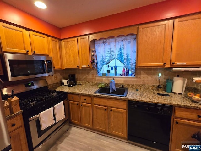 kitchen with stainless steel appliances, a sink, backsplash, and light stone countertops