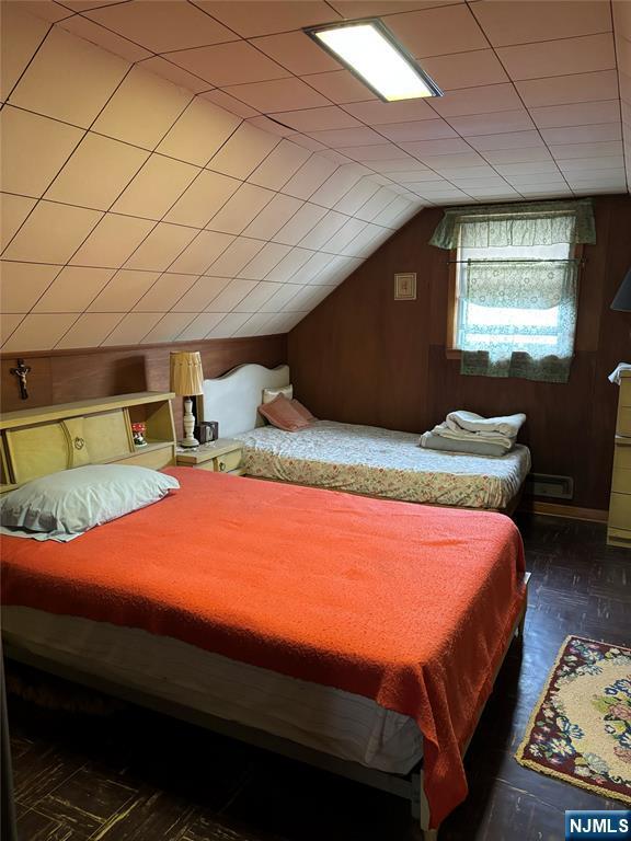 bedroom with vaulted ceiling, wooden walls, and wood finished floors