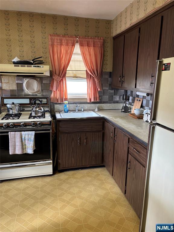 kitchen with gas stove, freestanding refrigerator, wallpapered walls, exhaust hood, and a sink