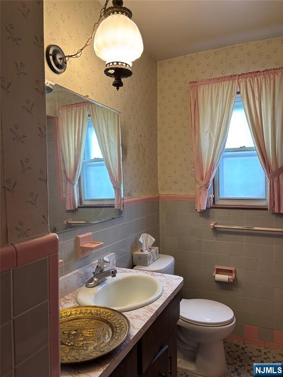 bathroom with toilet, wainscoting, vanity, tile walls, and healthy amount of natural light