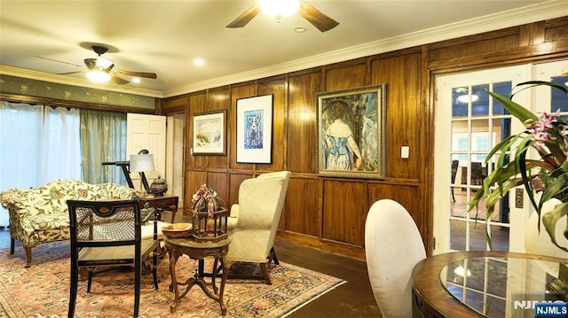 sitting room with a ceiling fan, ornamental molding, wood finished floors, and wooden walls