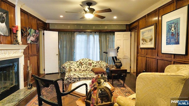 sitting room with crown molding, a ceiling fan, wooden walls, a glass covered fireplace, and wood finished floors