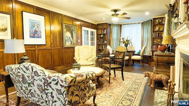 living area featuring ceiling fan, ornamental molding, a fireplace, and wooden walls
