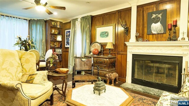 living area with a ceiling fan, a glass covered fireplace, ornamental molding, and wood finished floors