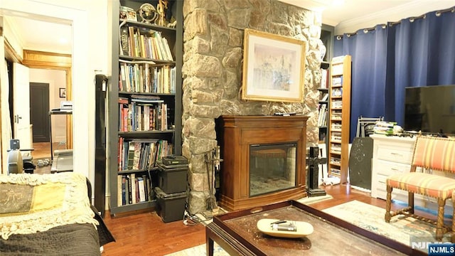 living area featuring crown molding, a stone fireplace, wood finished floors, and built in shelves