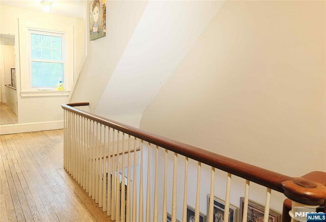 hallway featuring light wood-type flooring, an upstairs landing, and baseboards