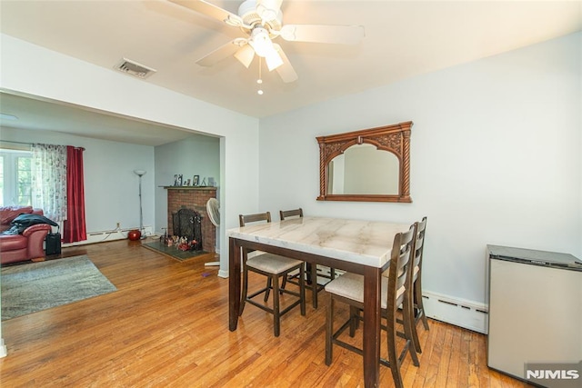 dining room with a baseboard heating unit, wood finished floors, ceiling fan, and a fireplace