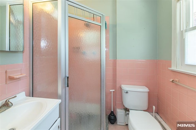 bathroom with tile walls, a shower stall, vanity, a wainscoted wall, and toilet