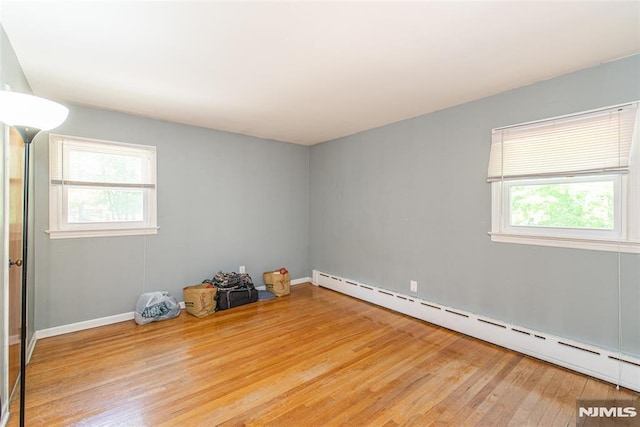 unfurnished room featuring a baseboard heating unit, wood finished floors, plenty of natural light, and baseboards