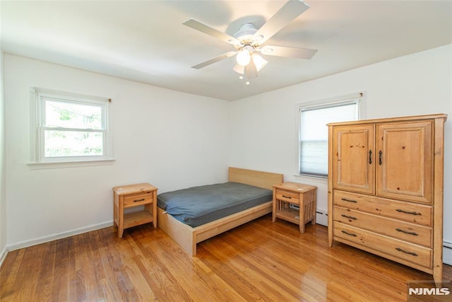 bedroom with light wood-style floors, baseboards, a baseboard radiator, and a ceiling fan