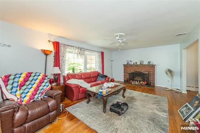 living room with a baseboard heating unit, a ceiling fan, wood finished floors, a brick fireplace, and baseboards