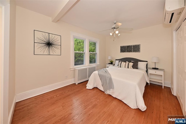 bedroom with radiator, an AC wall unit, light wood-style floors, and baseboards