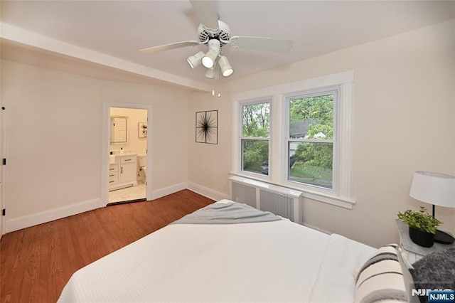 bedroom with baseboards, wood finished floors, ensuite bath, a ceiling fan, and radiator