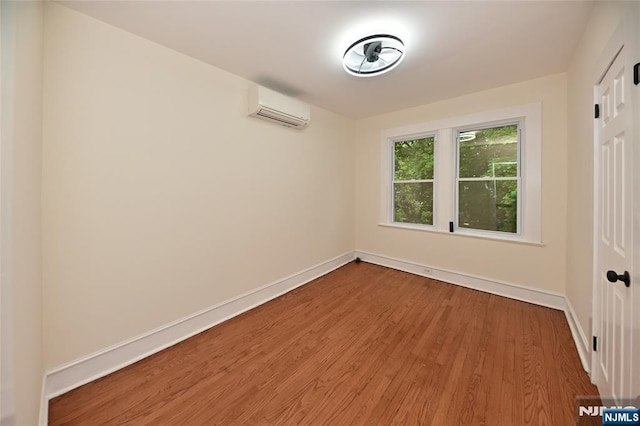 spare room featuring an AC wall unit, wood finished floors, and baseboards
