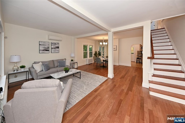 living room with arched walkways, a wall unit AC, stairs, wood finished floors, and baseboards