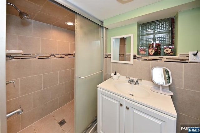 full bathroom with a stall shower, vanity, and tile walls