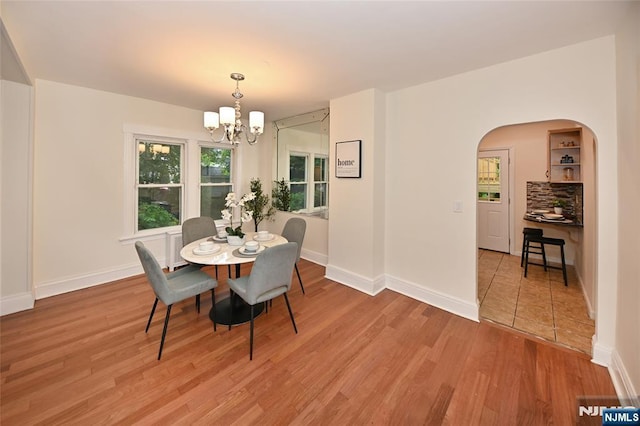 dining room with a chandelier, wood finished floors, arched walkways, and baseboards