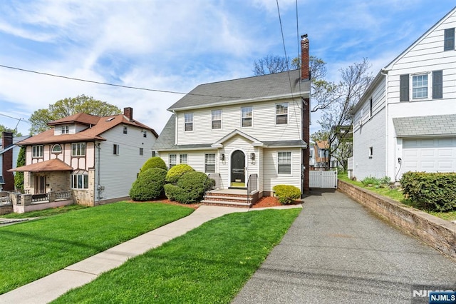 view of front of property with asphalt driveway, a chimney, a front lawn, and a residential view