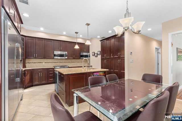 kitchen with appliances with stainless steel finishes, decorative backsplash, an island with sink, a sink, and light tile patterned floors