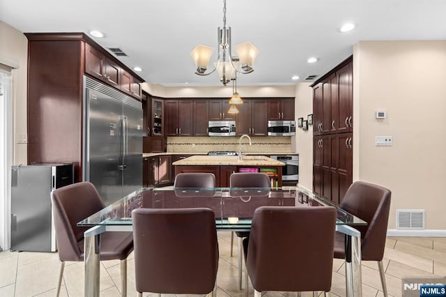 kitchen with appliances with stainless steel finishes, a chandelier, a center island with sink, decorative backsplash, and recessed lighting