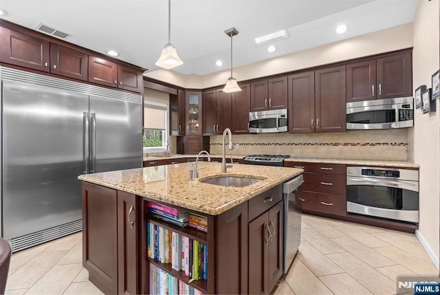 kitchen with appliances with stainless steel finishes, a sink, backsplash, light tile patterned flooring, and dark brown cabinetry