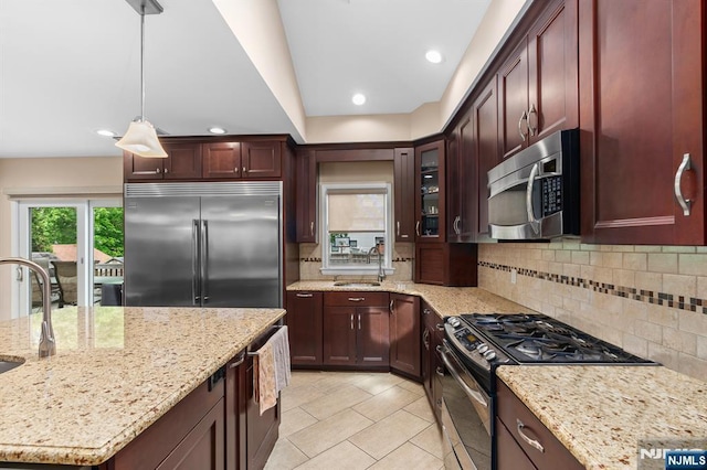 kitchen with appliances with stainless steel finishes, a sink, tasteful backsplash, decorative light fixtures, and light stone countertops