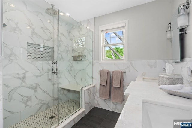 bathroom with a marble finish shower, double vanity, and tile walls