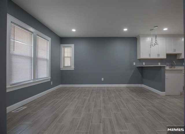 kitchen featuring white cabinets, a sink, baseboards, recessed lighting, and light wood-style floors