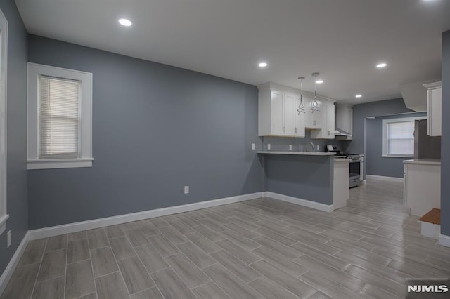 kitchen featuring gas range, a peninsula, white cabinetry, baseboards, and light countertops