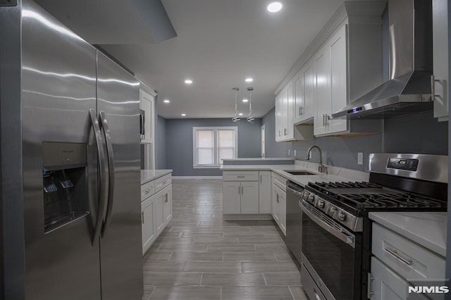 kitchen featuring stainless steel appliances, wall chimney exhaust hood, a sink, baseboards, and recessed lighting