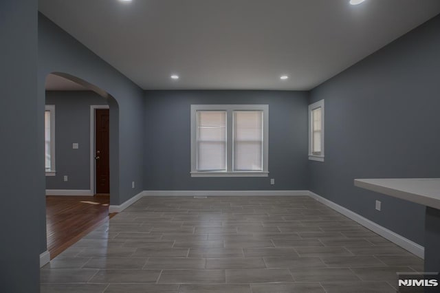 empty room featuring arched walkways, recessed lighting, wood finished floors, and baseboards