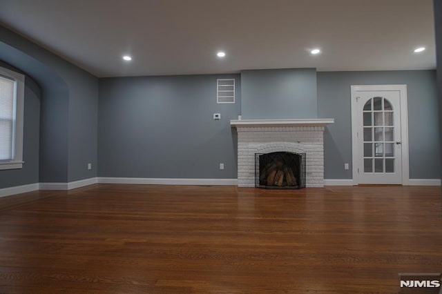 unfurnished living room with wood finished floors, a brick fireplace, baseboards, and recessed lighting
