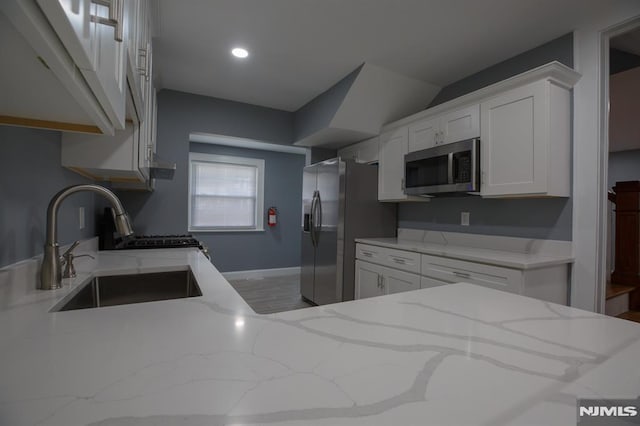 kitchen with stainless steel appliances, a sink, white cabinets, light stone countertops, and under cabinet range hood
