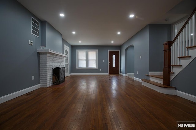 unfurnished living room with arched walkways, hardwood / wood-style flooring, a fireplace, recessed lighting, and stairs