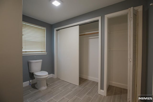 bathroom with toilet, wood finish floors, baseboards, and a closet