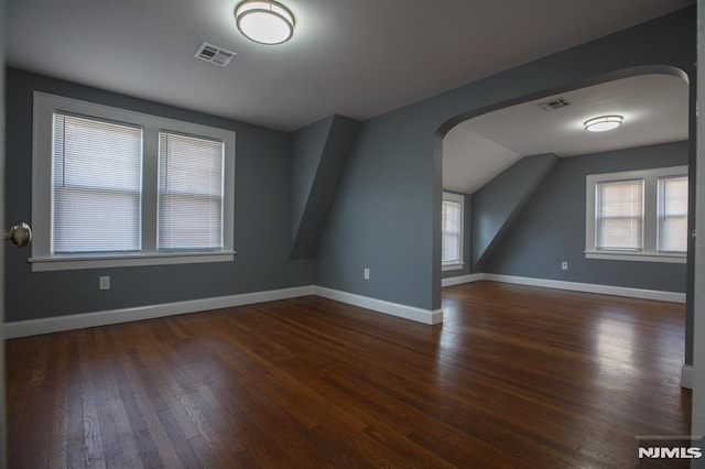 additional living space with wood finished floors, baseboards, arched walkways, and lofted ceiling