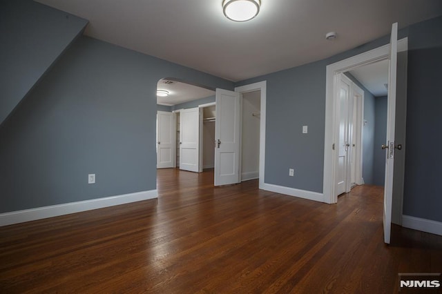 interior space featuring dark wood-type flooring, arched walkways, a smoke detector, and baseboards