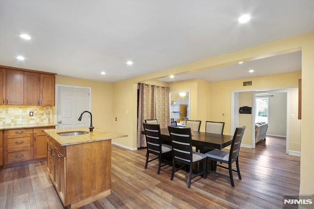 kitchen with a sink, hardwood / wood-style flooring, light stone counters, decorative backsplash, and brown cabinetry