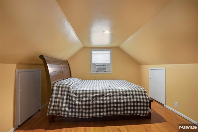 bedroom with cooling unit, wood finished floors, vaulted ceiling, and baseboards