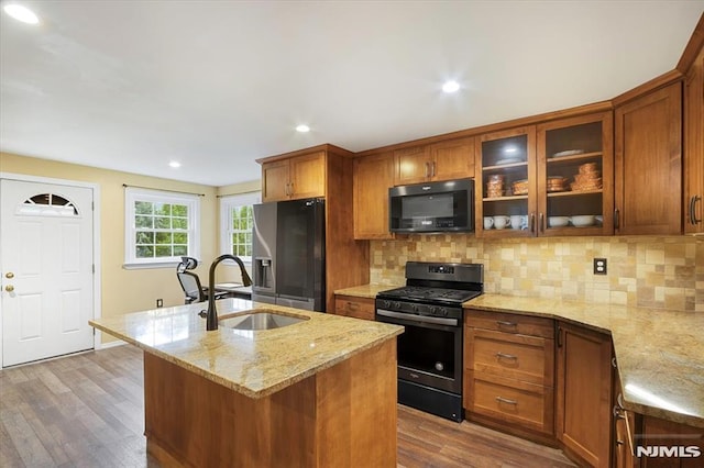 kitchen with black microwave, gas range oven, stainless steel refrigerator with ice dispenser, a sink, and wood finished floors