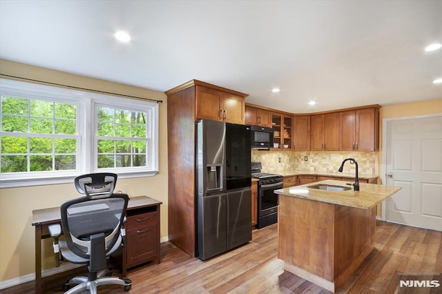 kitchen with a sink, black appliances, light stone counters, tasteful backsplash, and light wood-style flooring